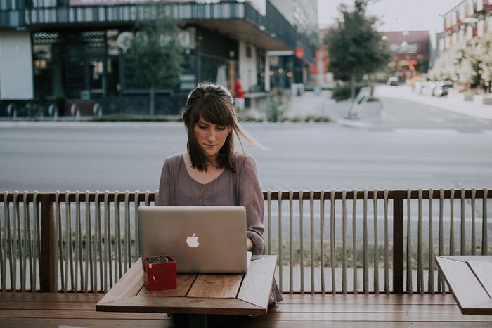 A photo of a patron using their laptop at an outdoor restaurant. Taken by Chritin Hume on Unsplash