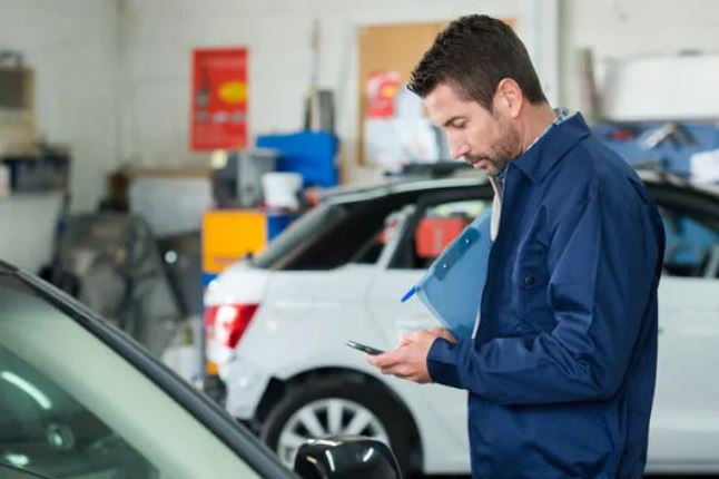 A mechanic double checks information on his phone before continuing with an automobile inspection