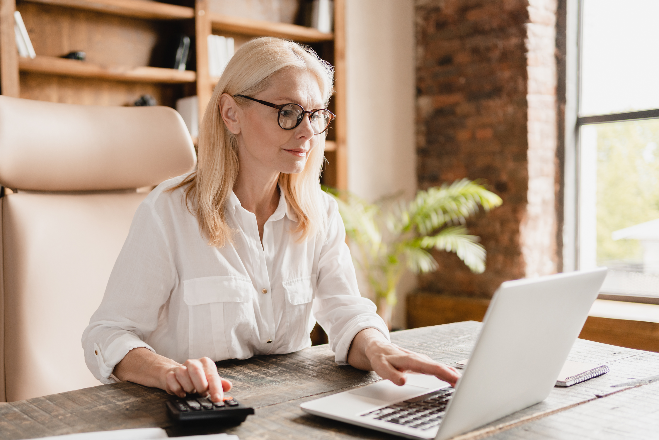 A person with blonde hair sits at a desk behind a computer