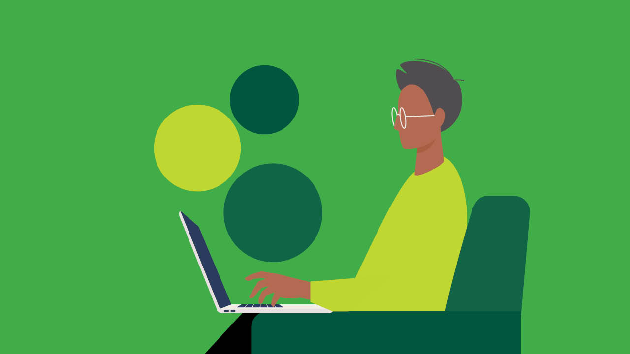 A man sits in front of a laptop in front of a green background